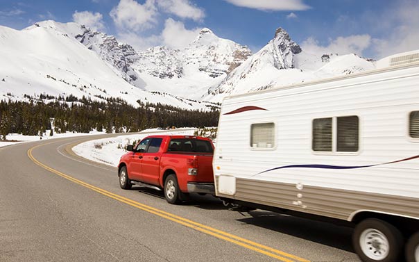 red SUV hauling travel trailer in snowy mountains