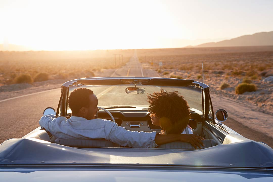 a couple in a convertible car driving down the highway at sunset